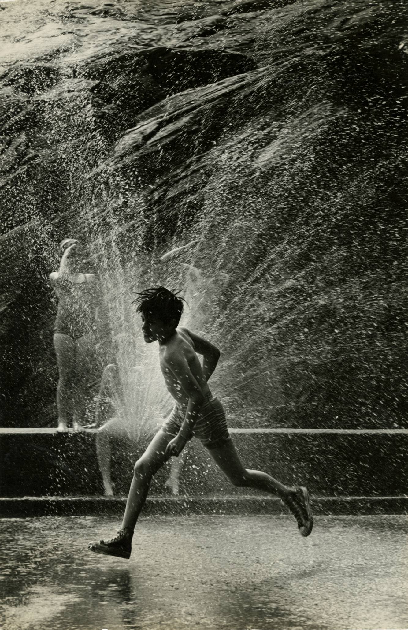 a boy in a bathing suit running through a spray of water